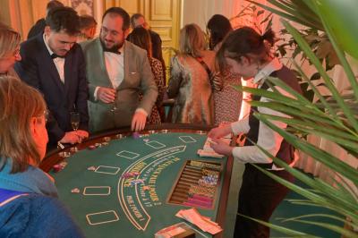 Table de jeu de casino avec tapis vert numéroté et porte-gobelets intégrés, entourée de personnes debout.