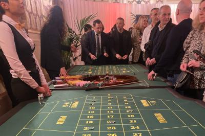 Table de jeu de casino avec tapis vert numéroté et porte-gobelets intégrés, entourée de personnes debout.