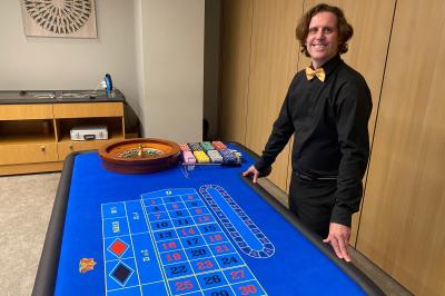 Table de jeu de casino avec tapis vert numéroté et porte-gobelets intégrés, entourée de personnes debout.