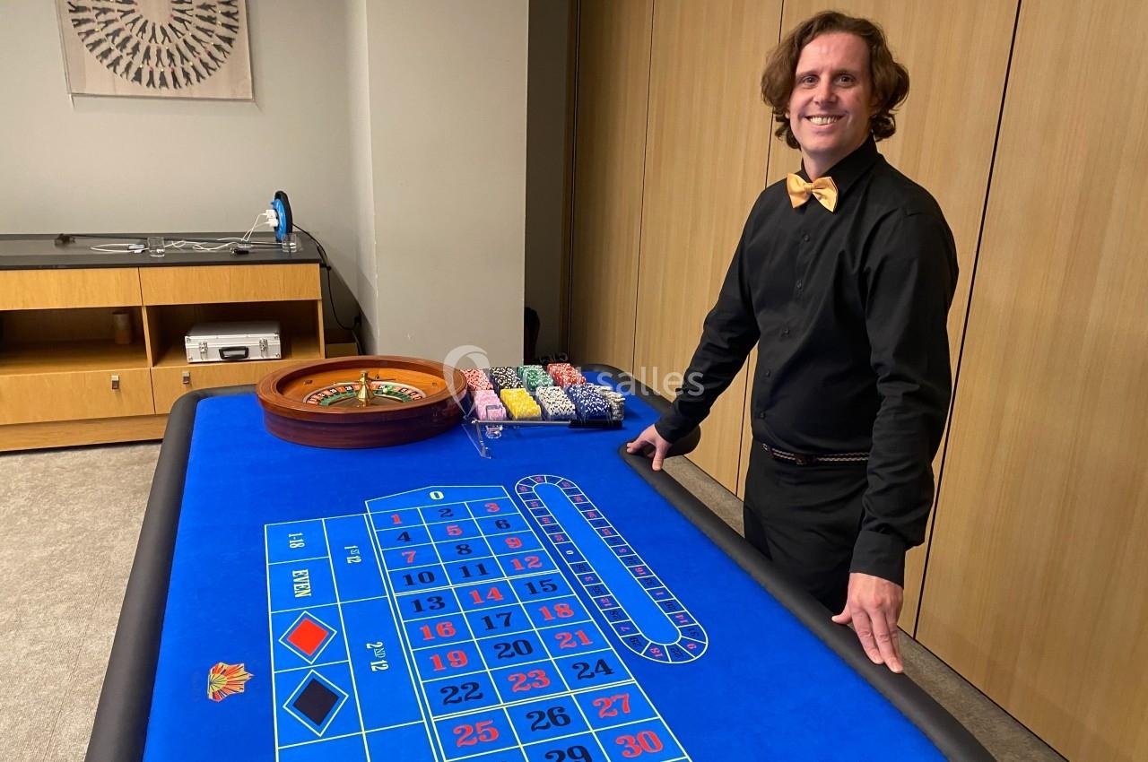 Un croupier souriant se tient près d'une table de roulette avec des jetons colorés alignés.