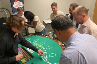 Table de jeu de casino avec tapis vert numéroté et porte-gobelets intégrés, entourée de personnes debout.