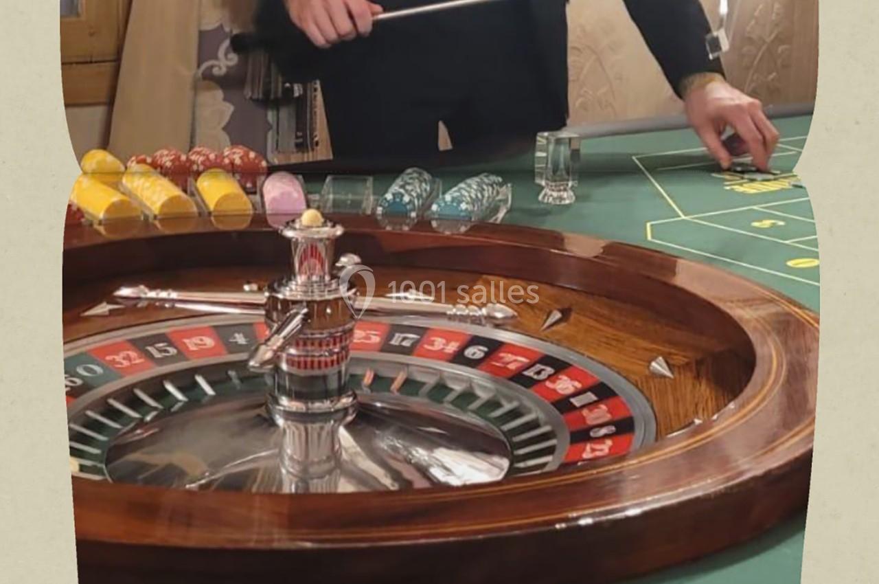 Roulette de casino en bois avec des jetons colorés et un croupier tenant un râteau sur la table de jeu.