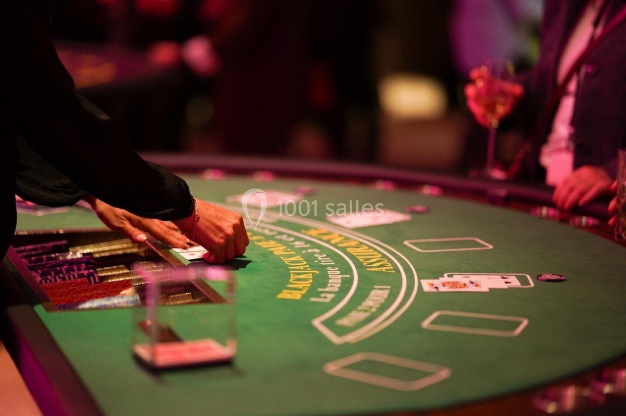 Personnes jouant au blackjack autour d'une table de casino éclairée, avec des cartes et des jetons visibles.