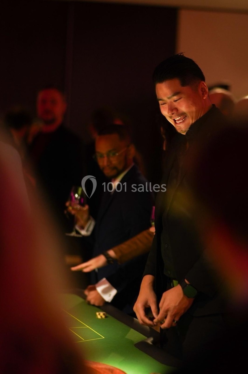 Un homme souriant joue à une table de casino entouré d'autres personnes dans une ambiance tamisée.