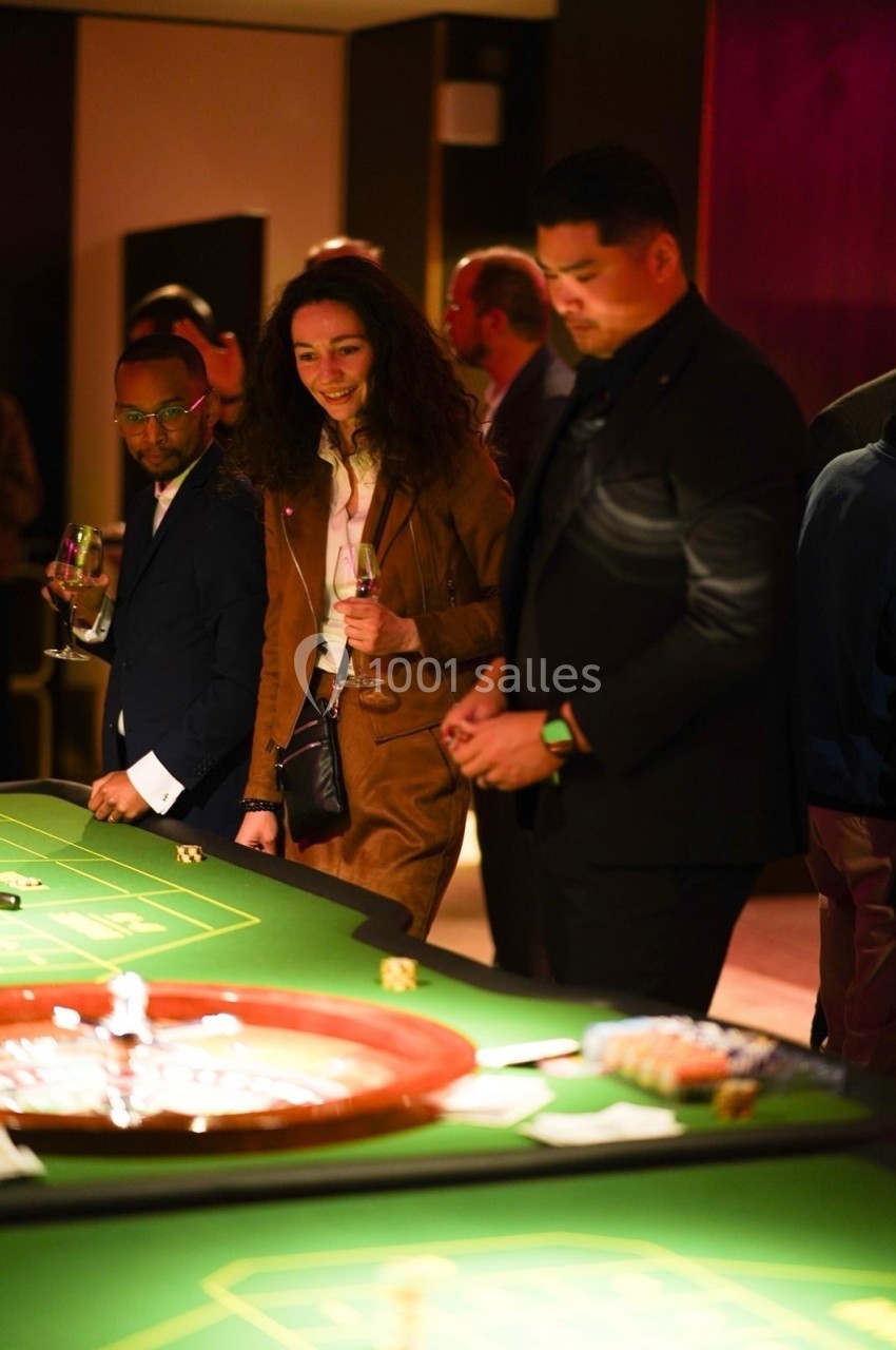 Des personnes élégamment vêtues jouent à une table de roulette dans un casino, tenant des verres à la main.
