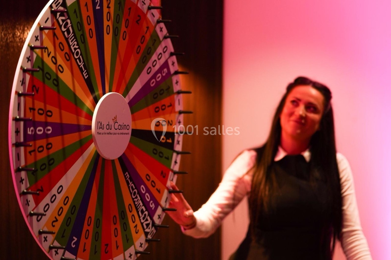 Une femme tourne une roue colorée de jeu avec des chiffres dans un environnement éclairé en rose.