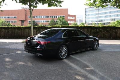 Voiture de luxe grise avec portes ouvertes, intérieur beige, stationnée devant un bâtiment moderne vitré.