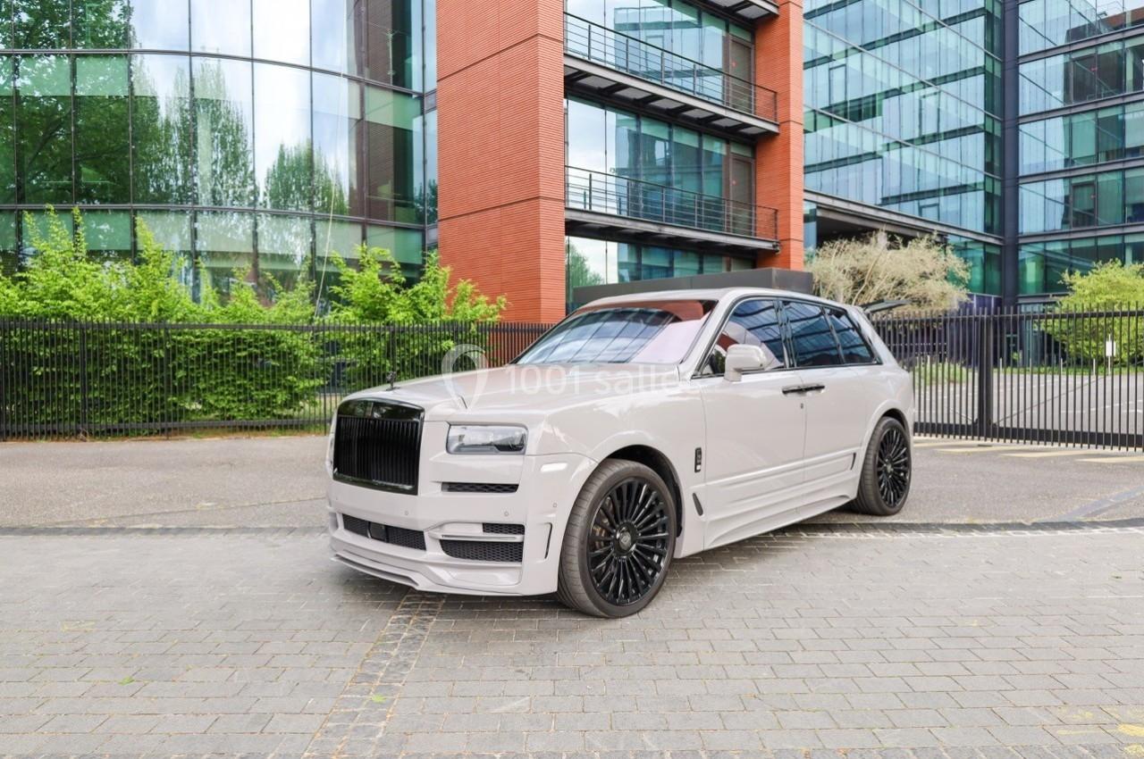SUV blanc garé devant un bâtiment moderne avec des façades en verre et des arbres en arrière-plan.