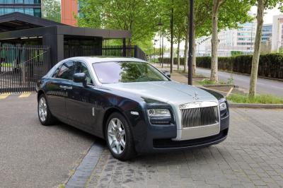 Voiture de luxe grise avec portes ouvertes, intérieur beige, stationnée devant un bâtiment moderne vitré.