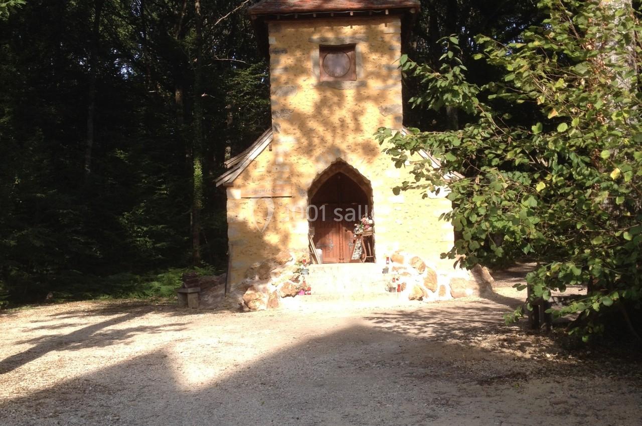 Petite chapelle en pierre avec un toit en pente, entourée d'arbres et éclairée par la lumière du soleil.