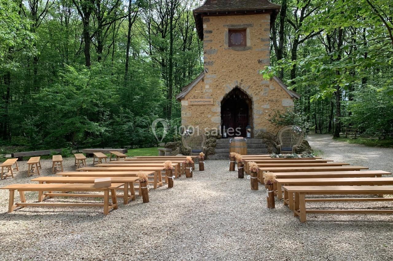 Petite chapelle en pierre entourée d'arbres, avec des bancs en bois disposés pour une cérémonie en plein air.