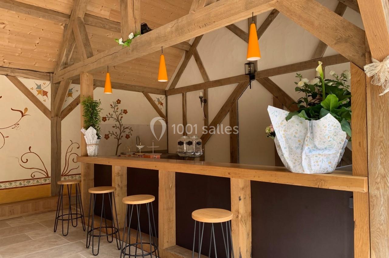 Bar en bois avec tabourets hauts, éclairé par des suspensions orange, entouré de plantes et décor mural floral.
