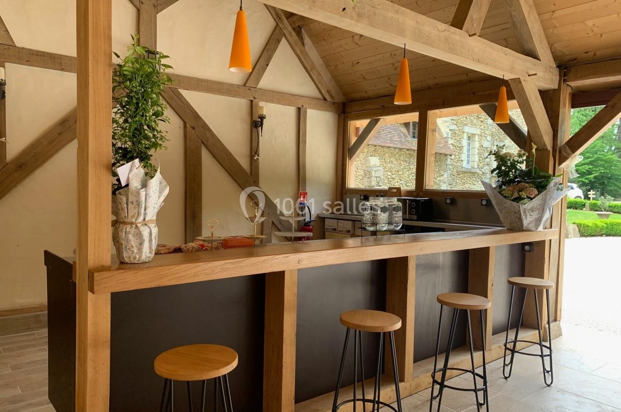 Bar en bois avec tabourets hauts, éclairage suspendu et vue sur un extérieur verdoyant à travers une ouverture.
