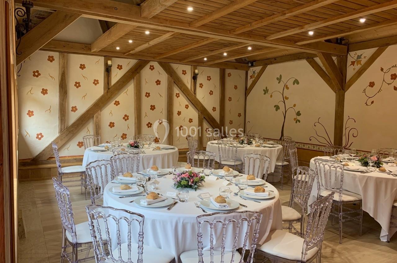 Salle de réception avec tables rondes dressées, chaises transparentes et décorations murales florales.