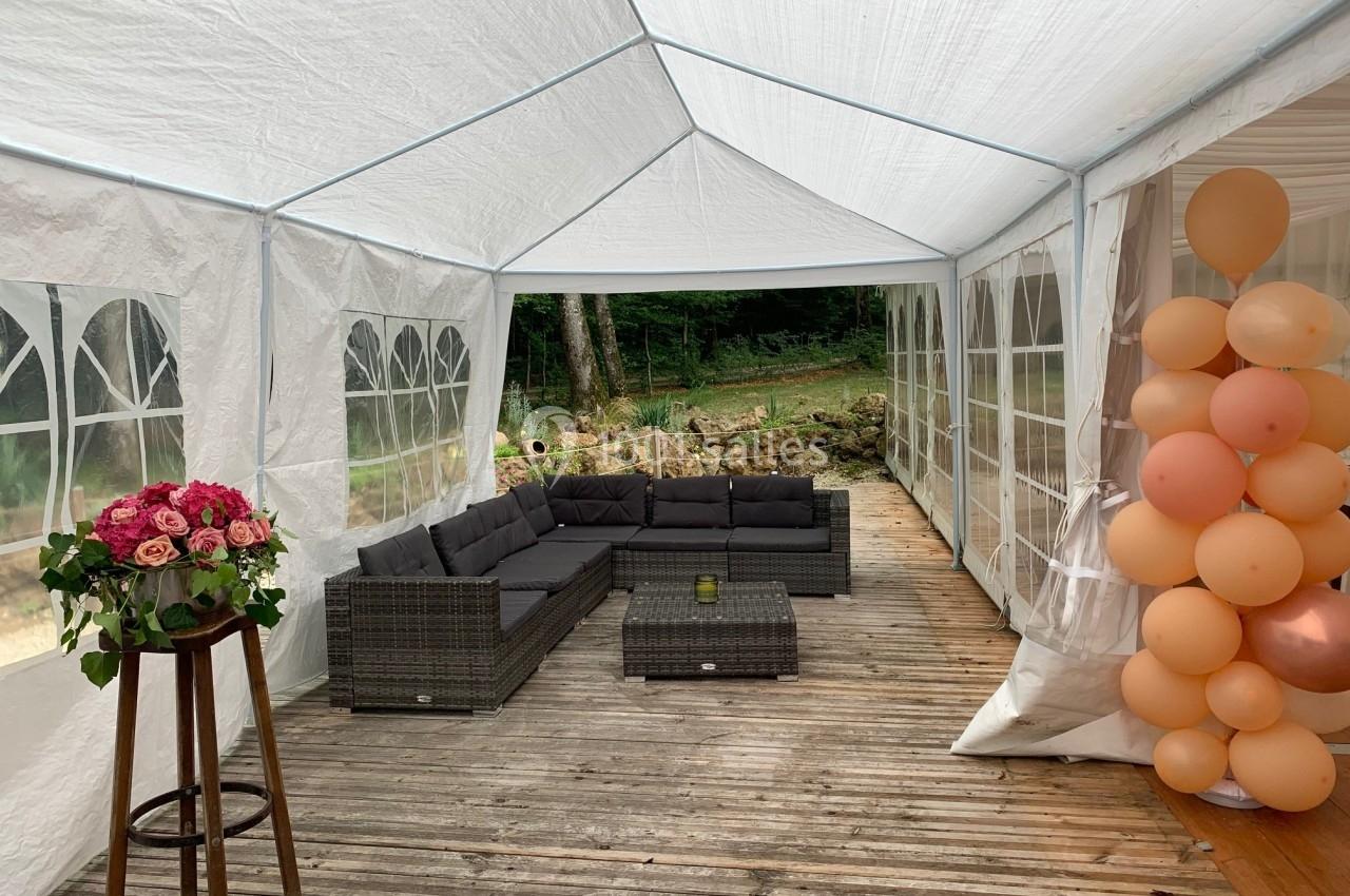 Intérieur d'une tente blanche avec salon de jardin en rotin, bouquet de fleurs et décoration de ballons.