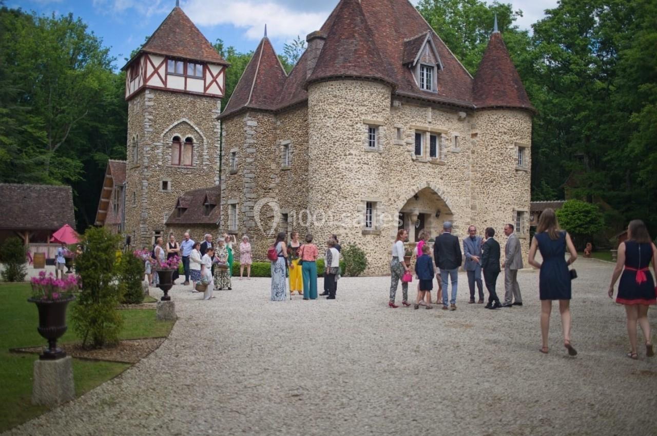 Groupe de personnes rassemblées devant un château en pierre entouré de verdure, par une journée ensoleillée.