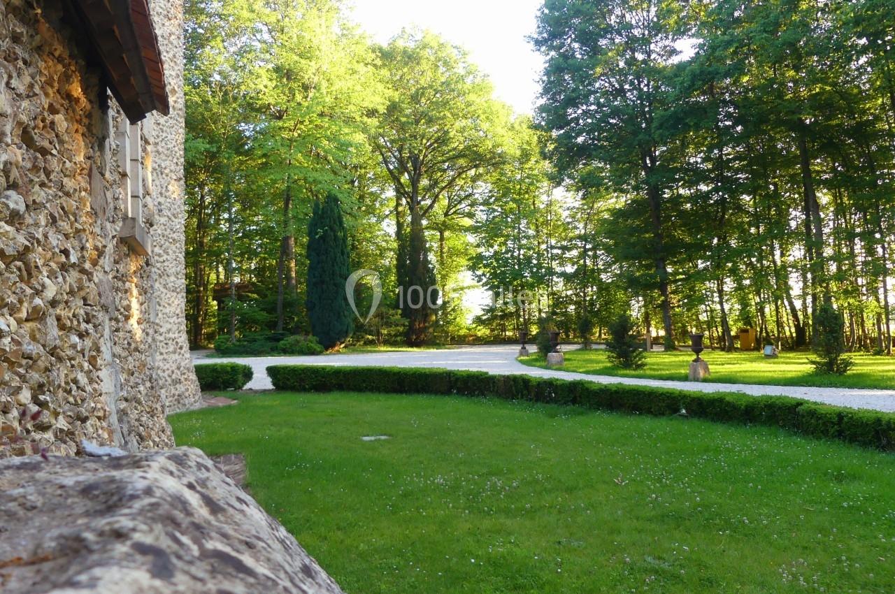 Vue d'un jardin verdoyant bordé d'arbres, avec une allée gravillonnée près d'un bâtiment en pierre.