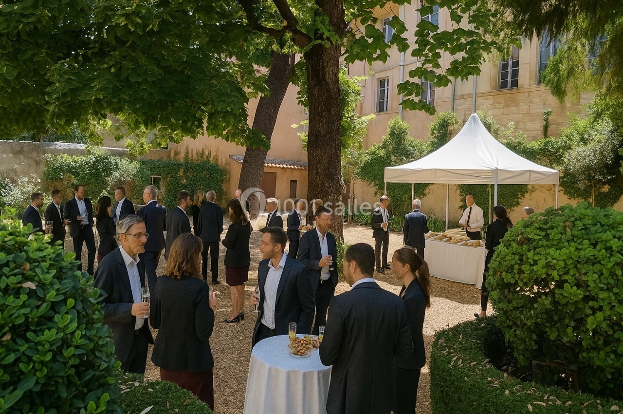 Groupe de personnes en tenue professionnelle discutant dans un jardin sous des arbres, près d'une table et d'un buffet sous…