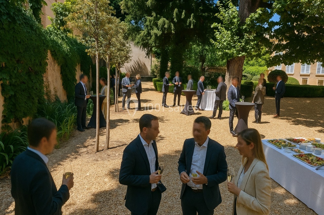Personnes en tenue professionnelle discutant et partageant un verre dans un jardin lors d'un événement en plein air.