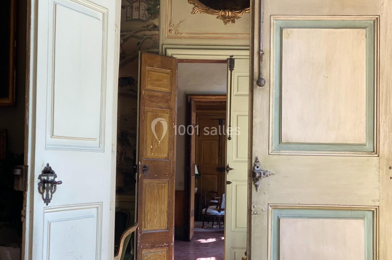 Portes anciennes ouvertes en enfilade révélant un intérieur lumineux avec parquet et décorations murales.