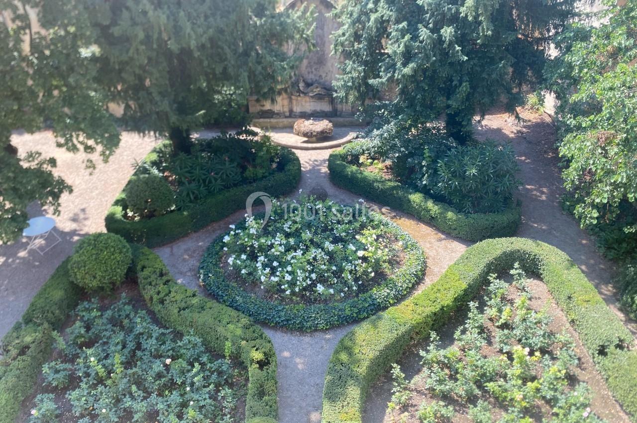 Vue d'un jardin symétrique avec parterres de fleurs, haies taillées et une fontaine en arrière-plan.
