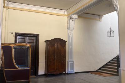 Hall d'entrée avec murs clairs, meubles en bois ancien et escalier montant à droite.