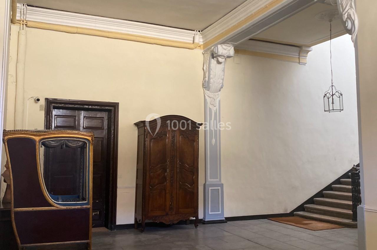 Hall d'entrée avec murs clairs, meubles en bois ancien et escalier montant à droite.
