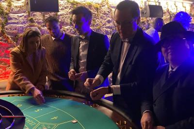 Table de jeu de casino avec tapis vert numéroté et porte-gobelets intégrés, entourée de personnes debout.