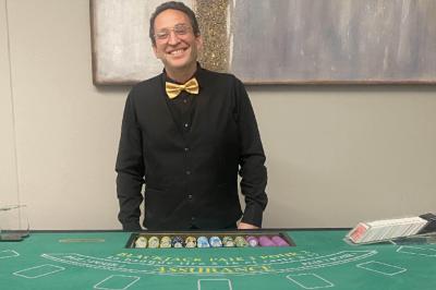 Table de jeu de casino avec tapis vert numéroté et porte-gobelets intégrés, entourée de personnes debout.