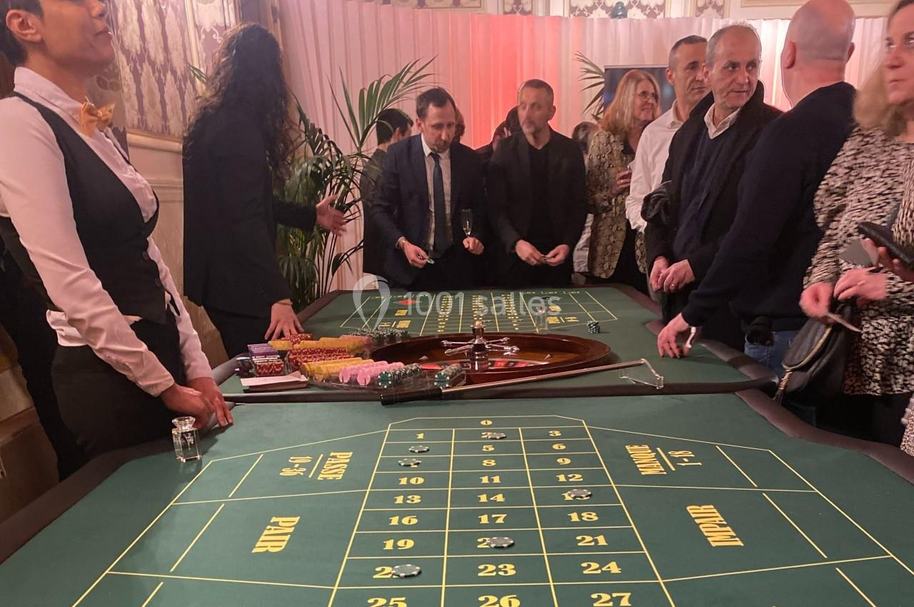 Des personnes rassemblées autour d'une table de roulette dans un casino, avec des jetons et une roue visible.