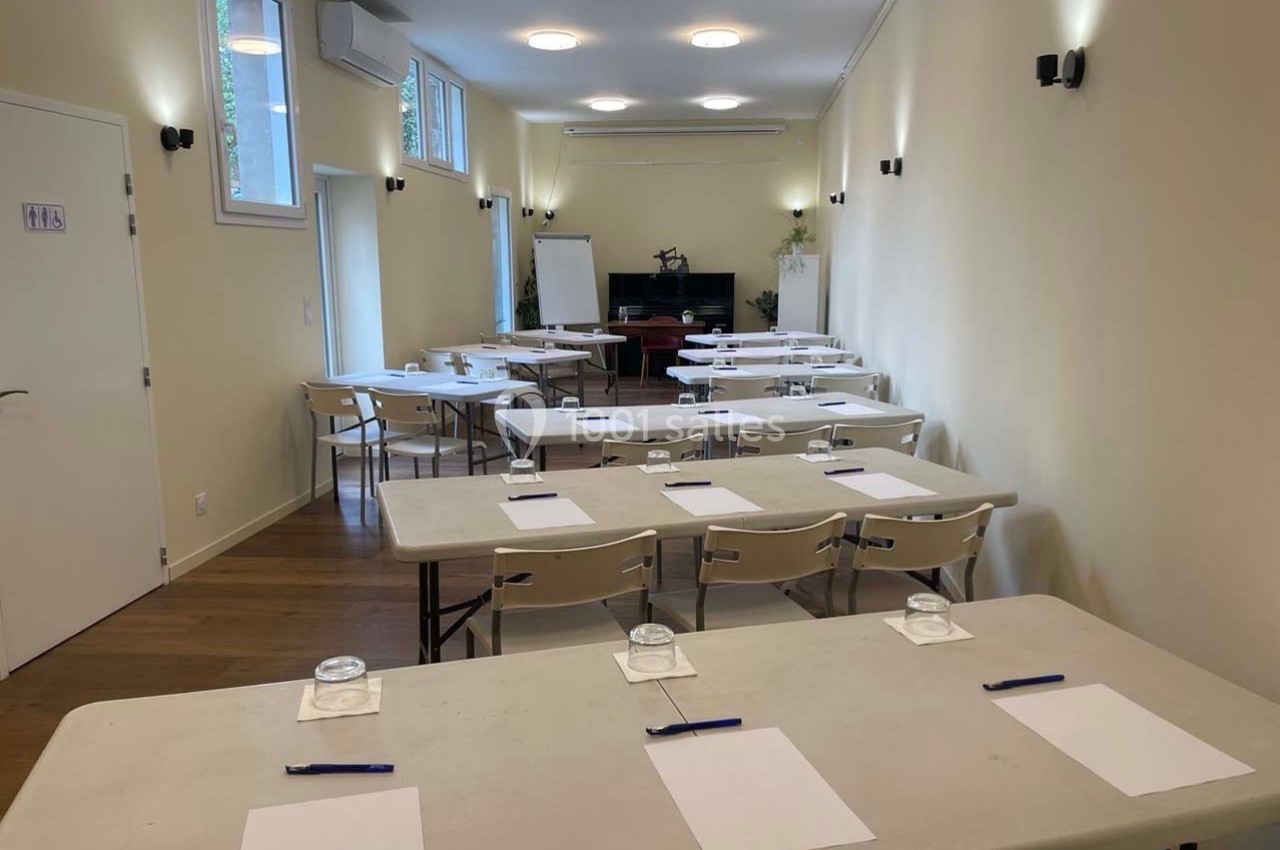 Salle lumineuse aménagée avec des tables, chaises, blocs-notes, stylos et verres, prête pour une réunion ou un atelier.