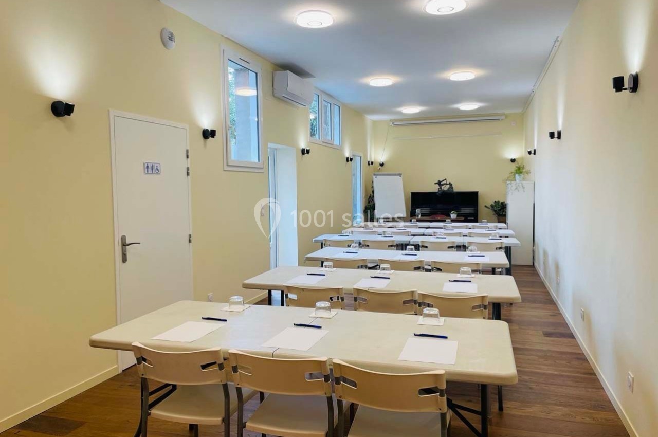 Salle de réunion lumineuse avec des tables alignées, des chaises, des blocs-notes et un tableau blanc au fond.