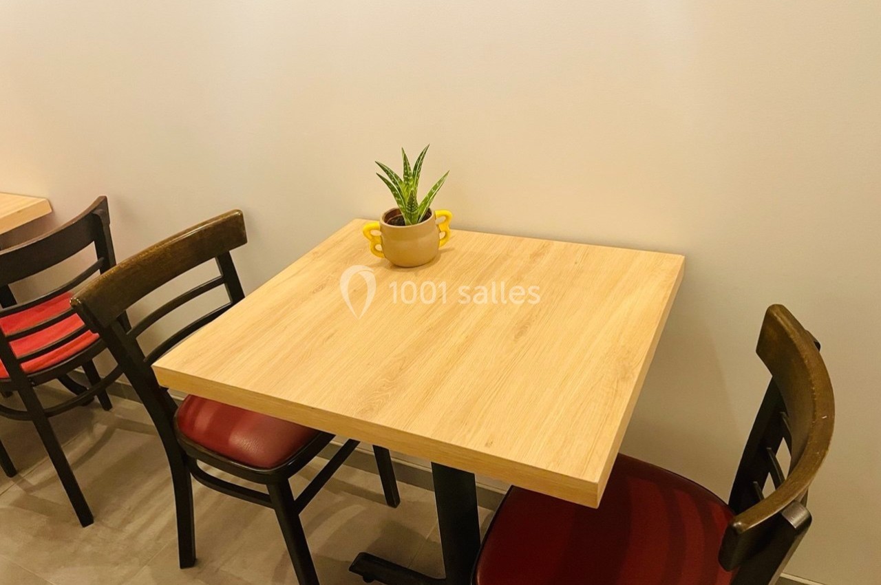 Table en bois clair avec une petite plante en pot au centre, entourée de deux chaises à assise rouge.