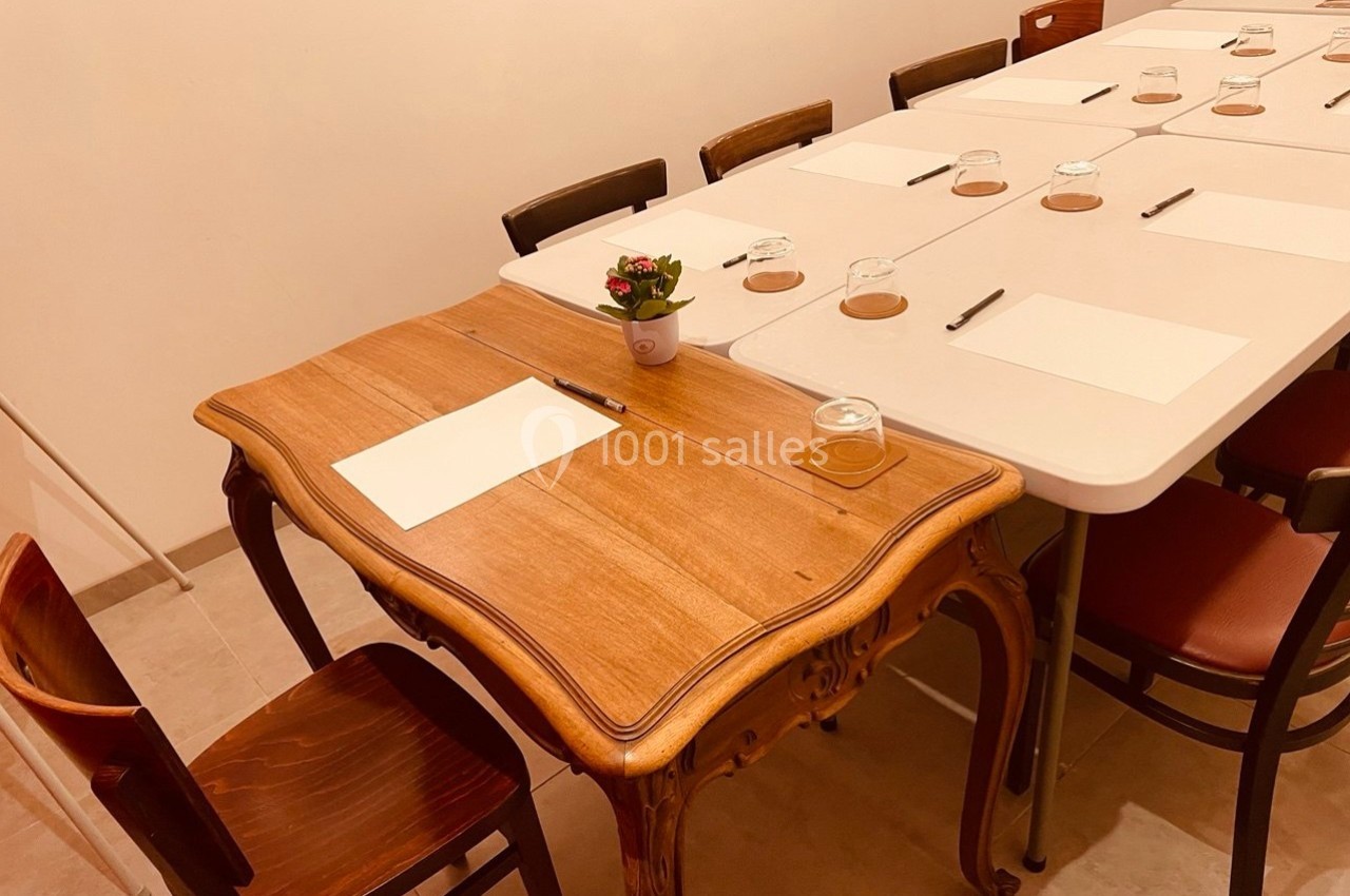 Table en bois ancien et table moderne alignées, équipées de feuilles, stylos et verres, dans une salle sobre.