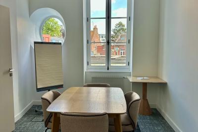Salle de réunion lumineuse avec table en bois, quatre chaises, un tableau de présentation et une fenêtre donnant sur des…