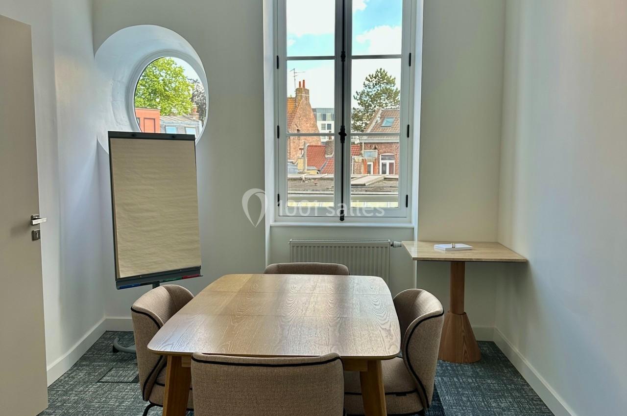 Salle de réunion lumineuse avec table en bois, quatre chaises, un tableau de présentation et une fenêtre donnant sur des…