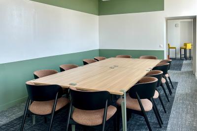 Salle de réunion lumineuse avec table en bois, quatre chaises, un tableau de présentation et une fenêtre donnant sur des…