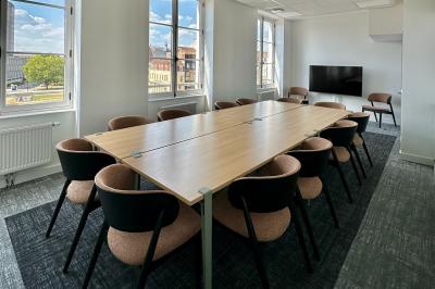 Salle de réunion lumineuse avec table en bois, quatre chaises, un tableau de présentation et une fenêtre donnant sur des…