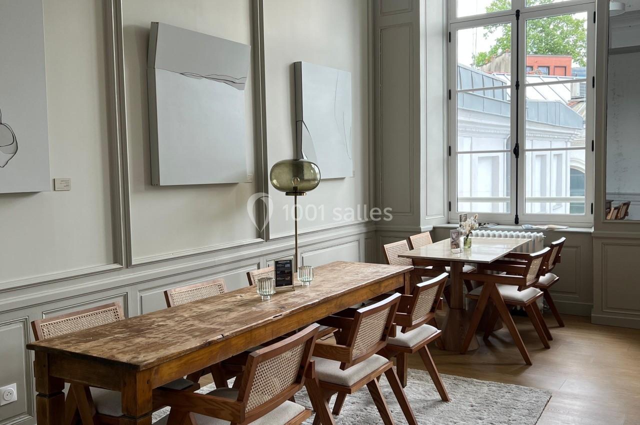 Salle à manger lumineuse avec table en bois, chaises en rotin, tapis clair et grande fenêtre donnant sur l'extérieur.