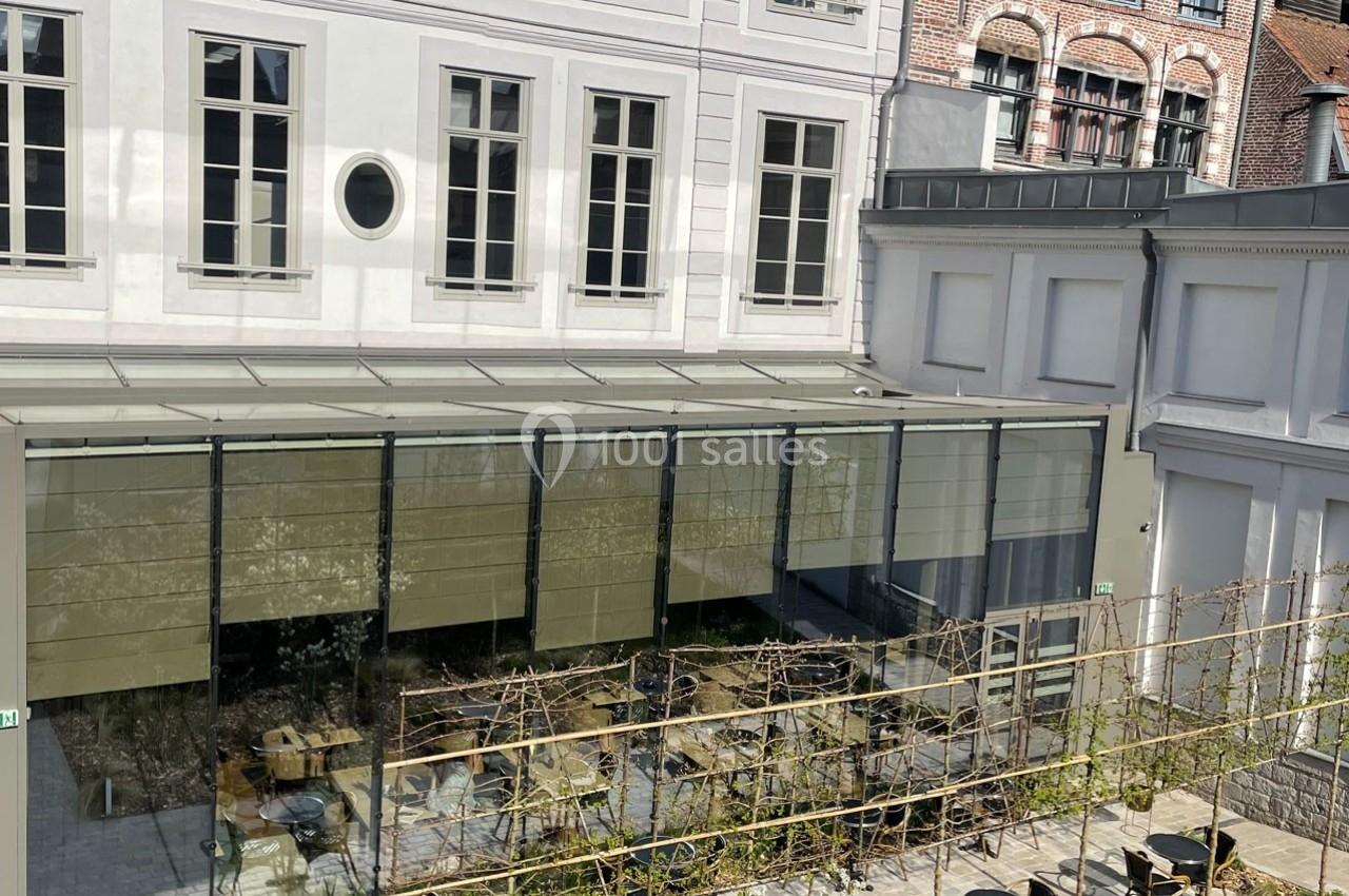 Terrasse extérieure d'un café avec tables et chaises, entourée de bâtiments en briques et en pierre blanche.