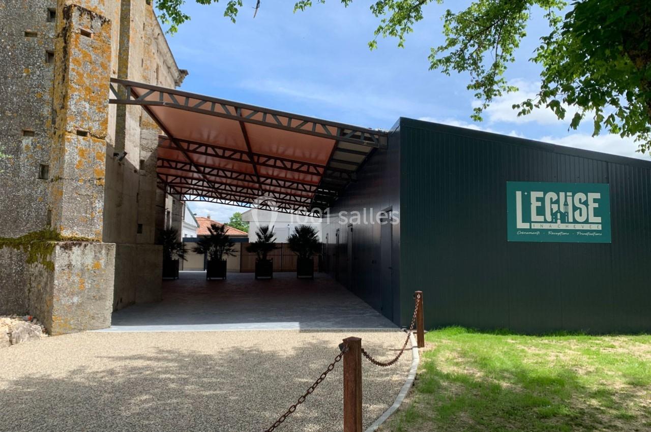 Entrée d'un bâtiment moderne attenant à une église ancienne, avec une structure métallique et des plantes en pots.