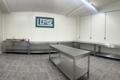 Salle équipée de plans de travail en inox, évier et carrelage gris, avec un panneau ’L'Eglise’ au mur.