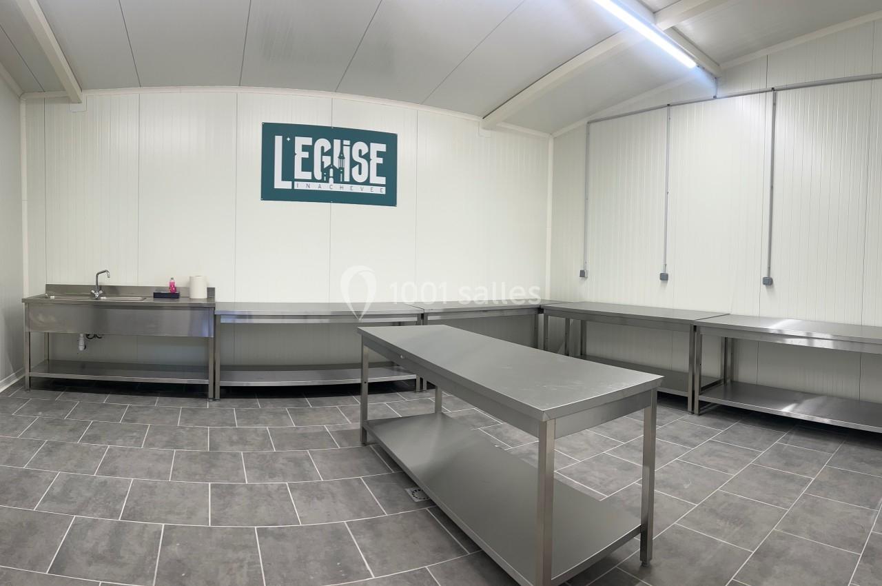 Salle équipée de plans de travail en inox, évier et carrelage gris, avec un panneau ’L'Eglise’ au mur.