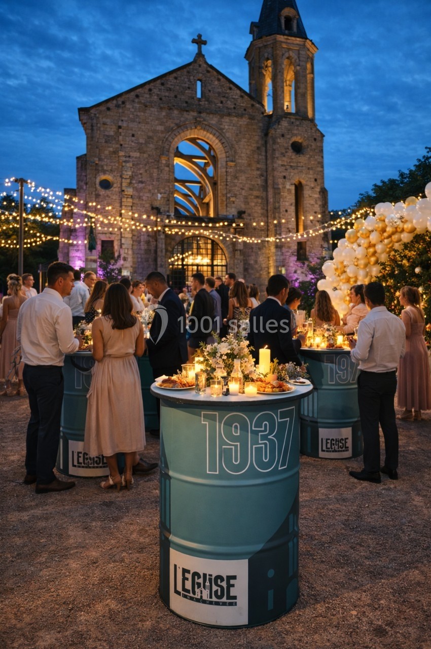 Personnes rassemblées autour de tables décorées, devant une église illuminée, sous des guirlandes lumineuses.