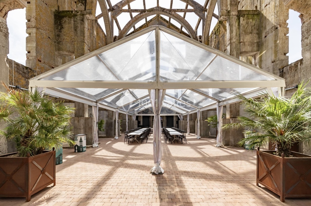 Structure transparente installée dans une ancienne bâtisse en pierre, avec des tables et des plantes en pot.