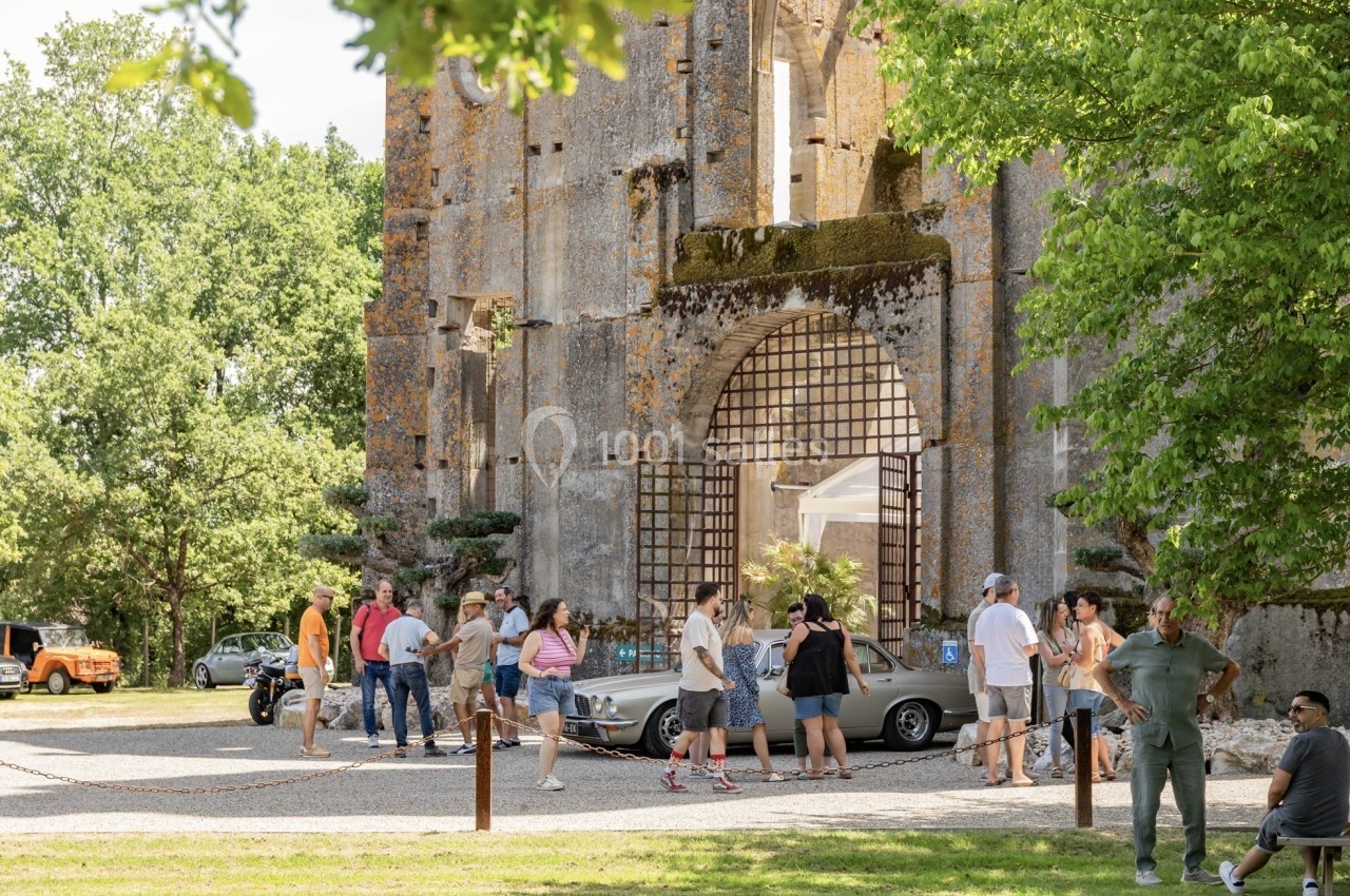 Des visiteurs se rassemblent devant les ruines d'un bâtiment historique entouré d'arbres et de voitures anciennes.