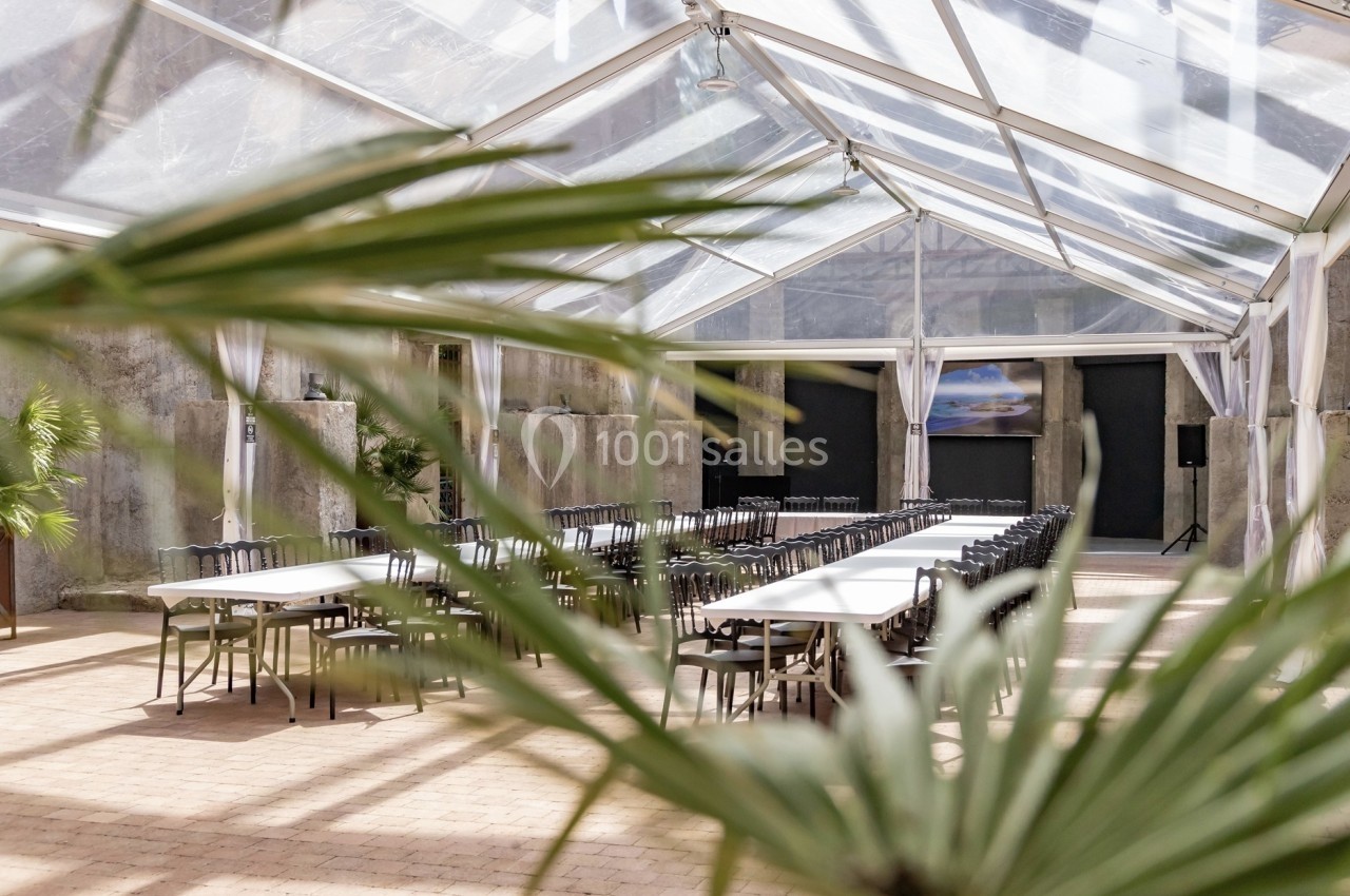 Salle de réunion lumineuse sous une verrière, avec de longues tables blanches et des chaises alignées.