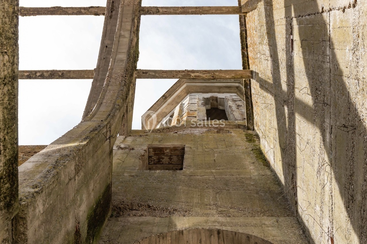 Vue en contre-plongée d'une structure en pierre partiellement en ruine avec des ouvertures et un ciel clair en arrière-plan.