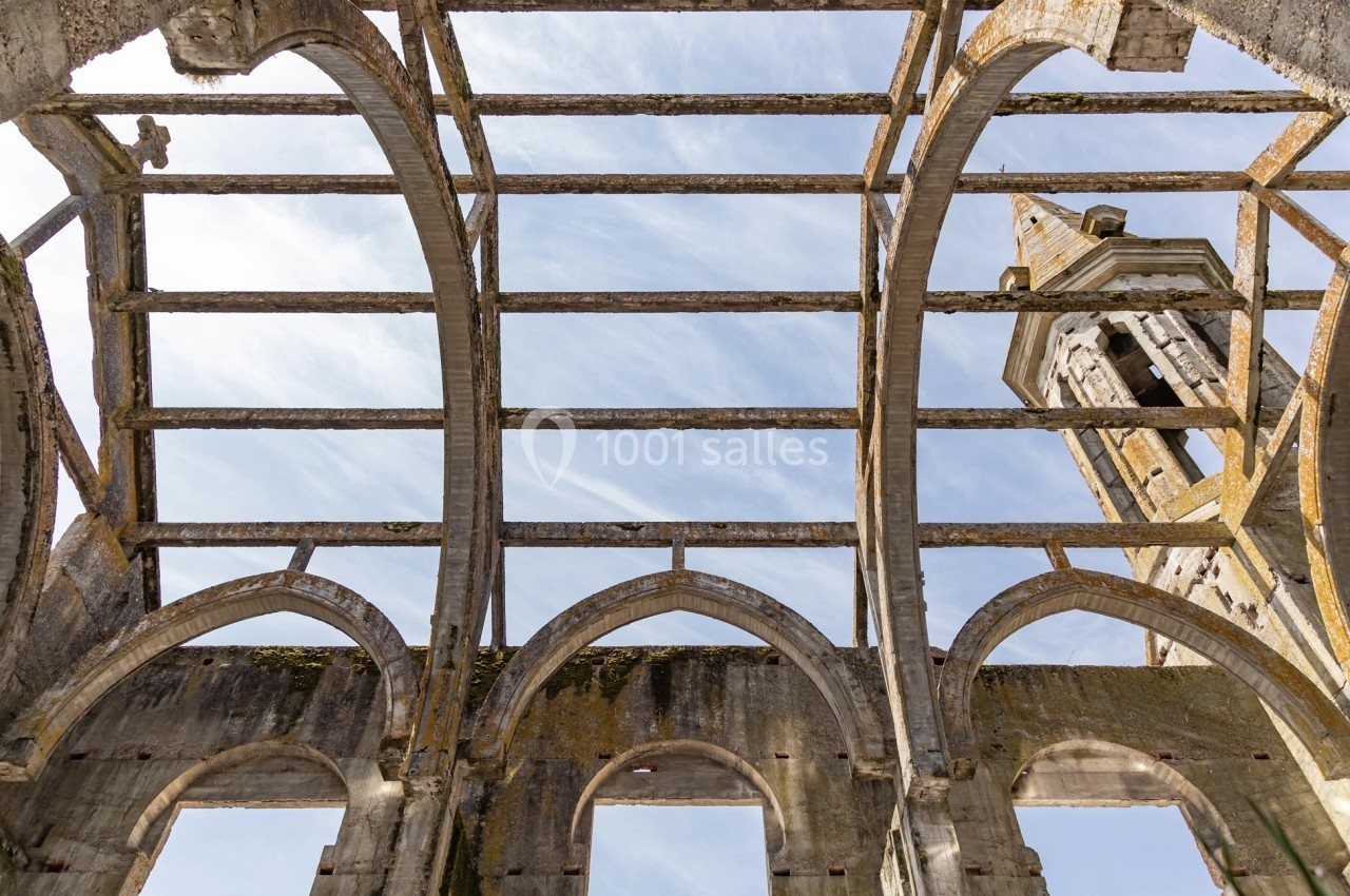 Structure en ruines avec des arcs en pierre et un clocher visible sous un ciel bleu.