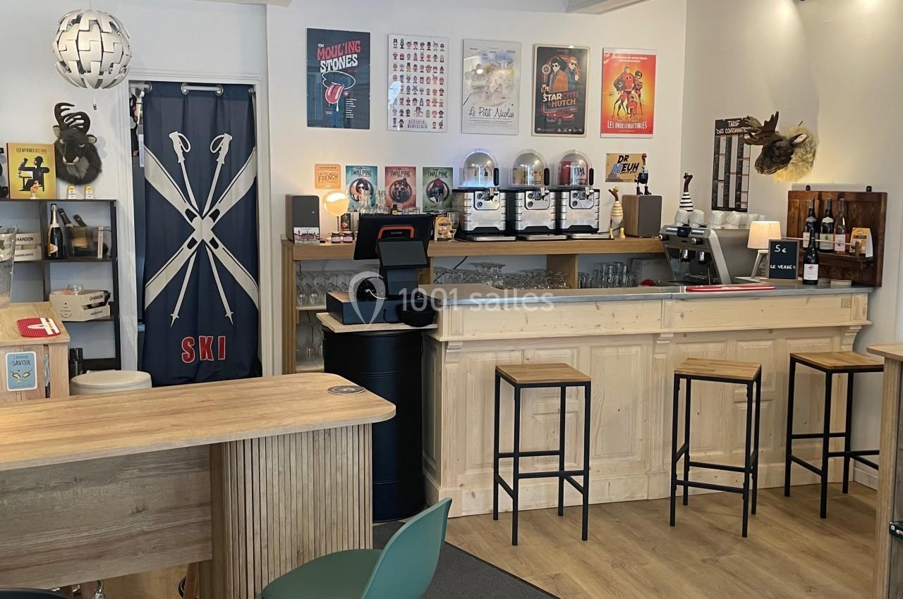 Intérieur d'un bar avec comptoir en bois, tabourets hauts, décorations murales et étagères exposant des produits.